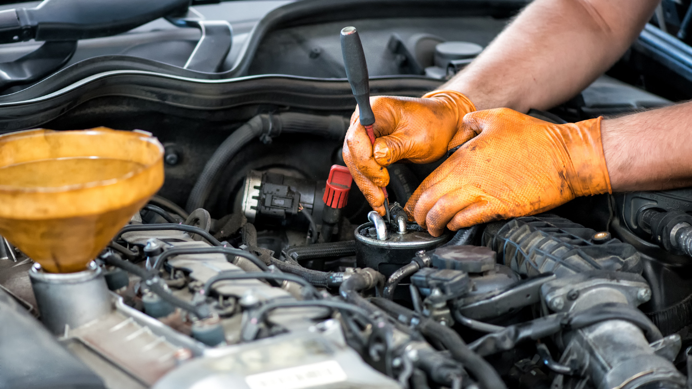 Mechanic in orange gloves checking a car engine with an oil funnel nearby