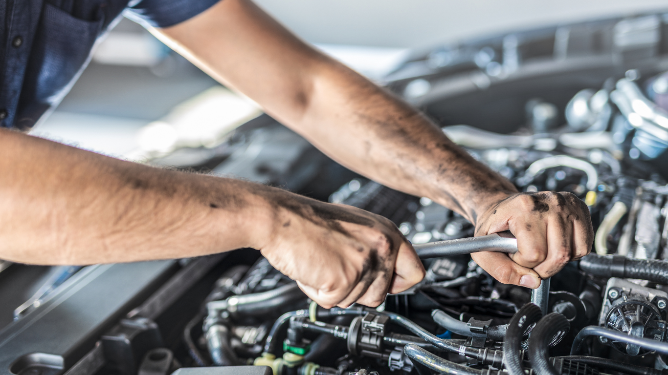 Mechanic using a wrench to repair an engine under an open car hood