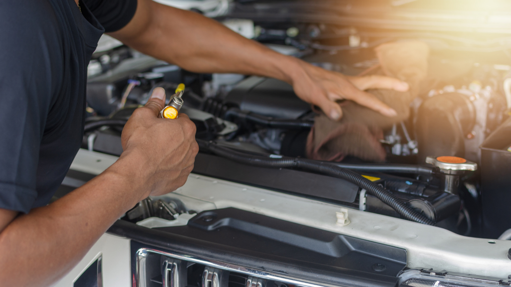 Mechanic inspecting engine bay with a wrench under bright workshop light