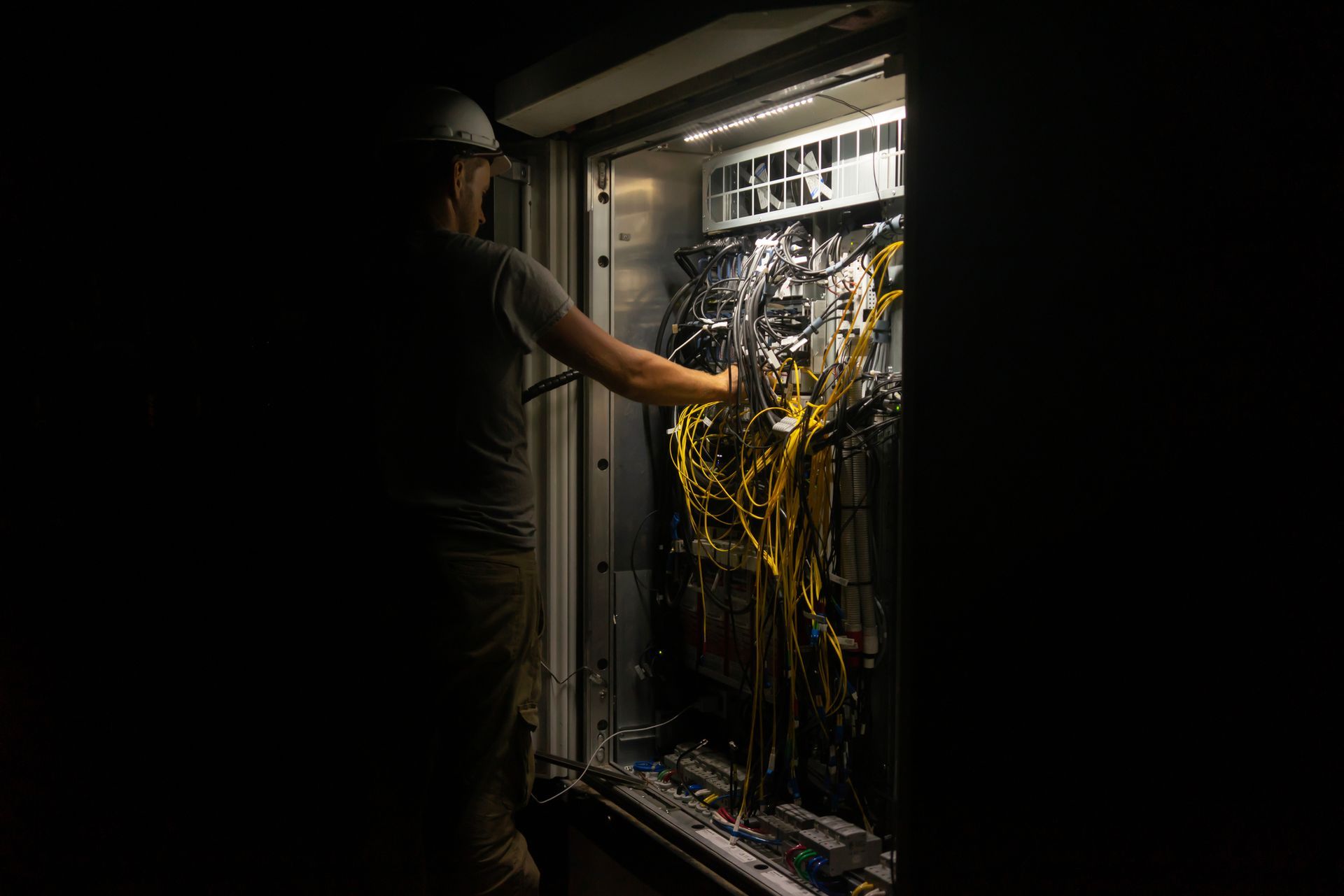 An electrical technician is working on the switchboard in a dark area