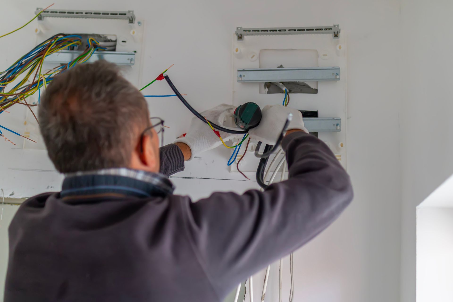 Person installing electrical wiring in a white wall panel with exposed wires Person installing electrical wiring in a white wall panel with exposed wires