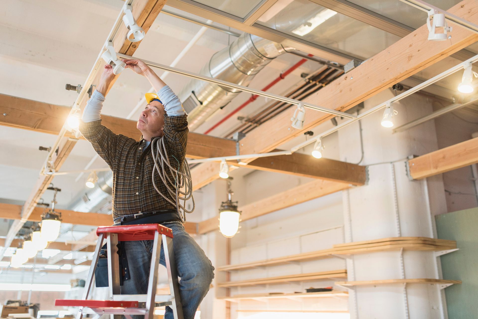 Electrician on a ladder installs lighting in a building Electrician on a ladder installs lighting in a building