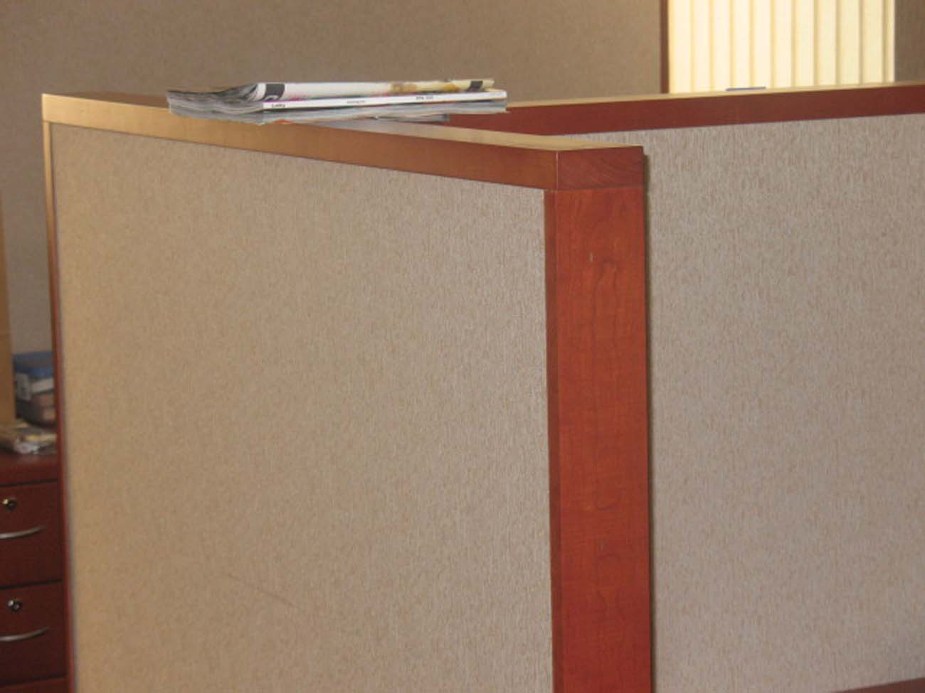 A cubicle with a wooden border and a stack of books on top of it