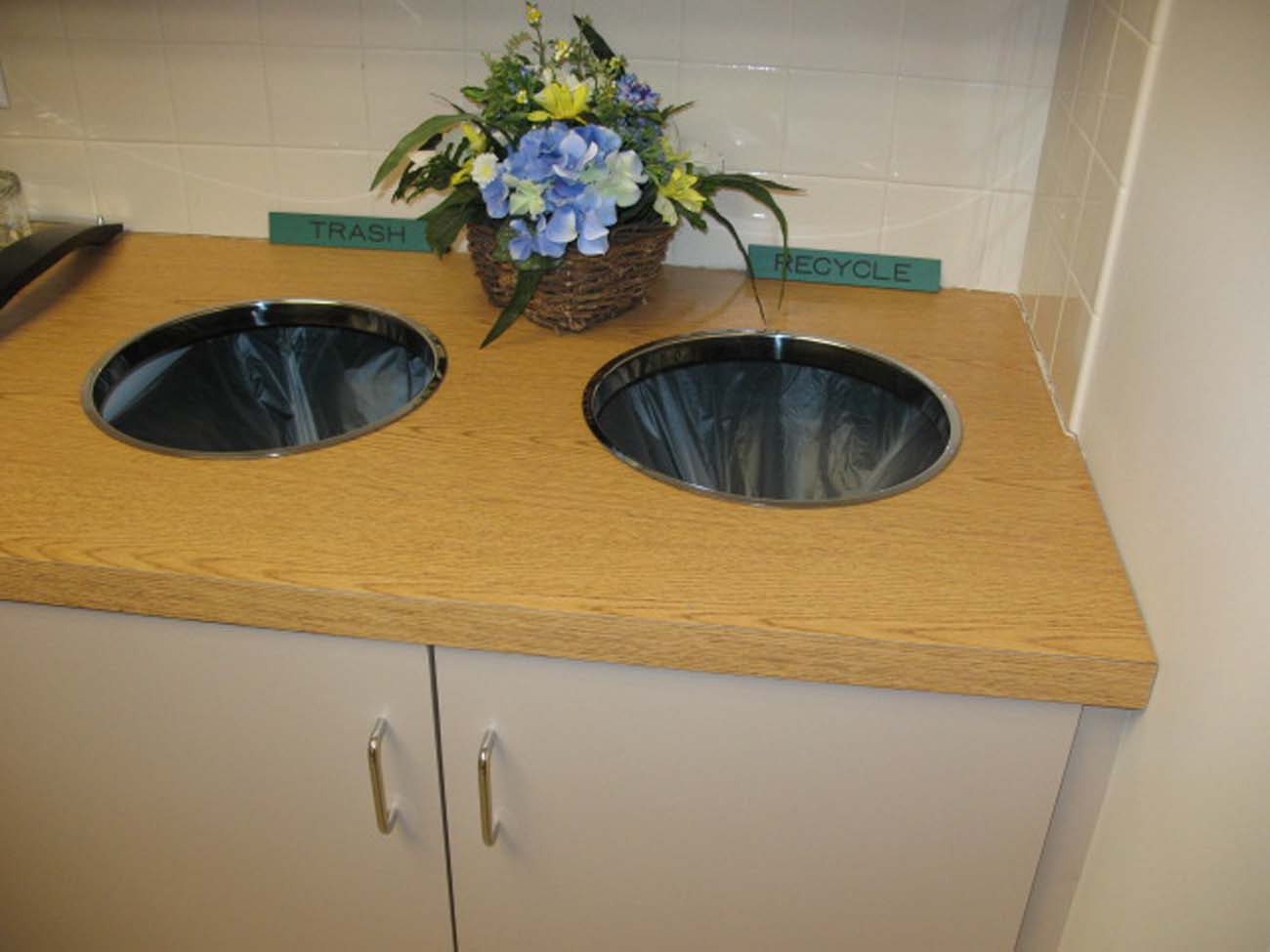 A recycling bin with a basket of flowers on top of it