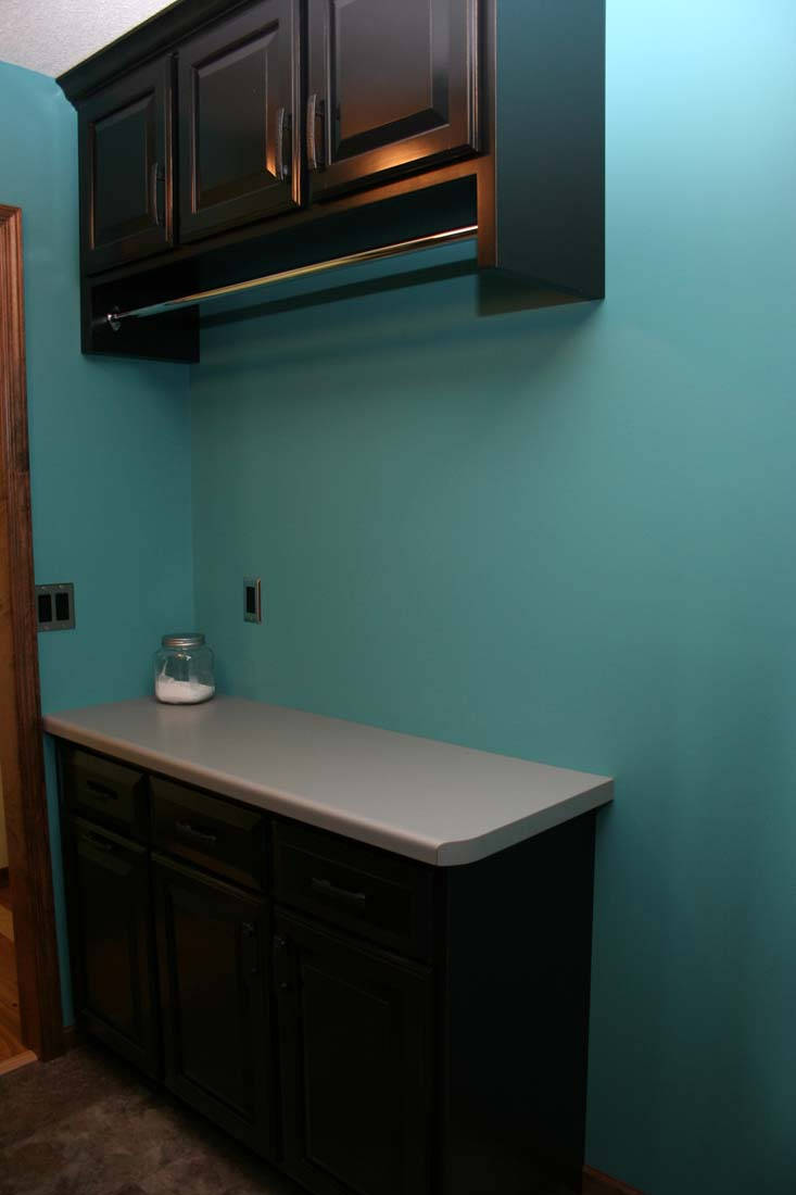 A laundry room with blue walls and black cabinets
