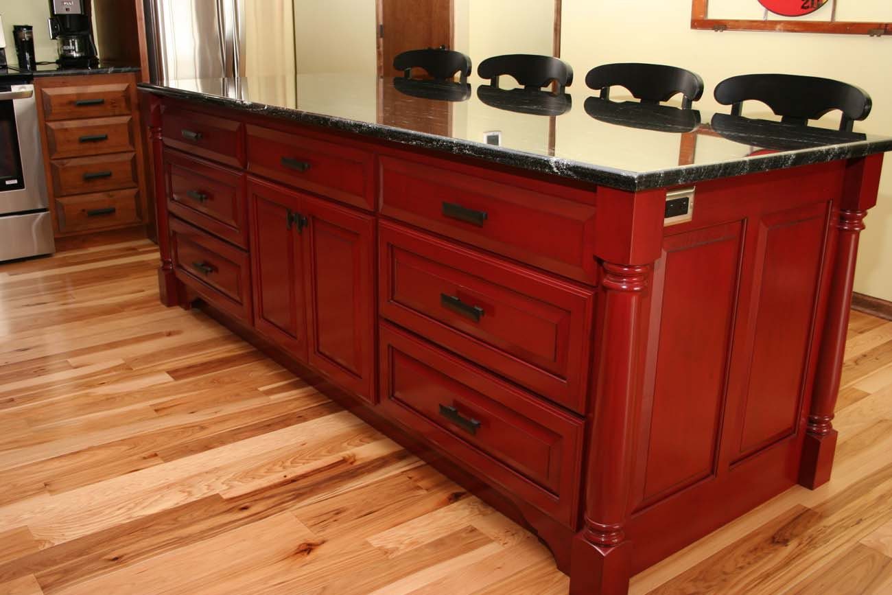 A kitchen island with red cabinets and black granite counter tops
