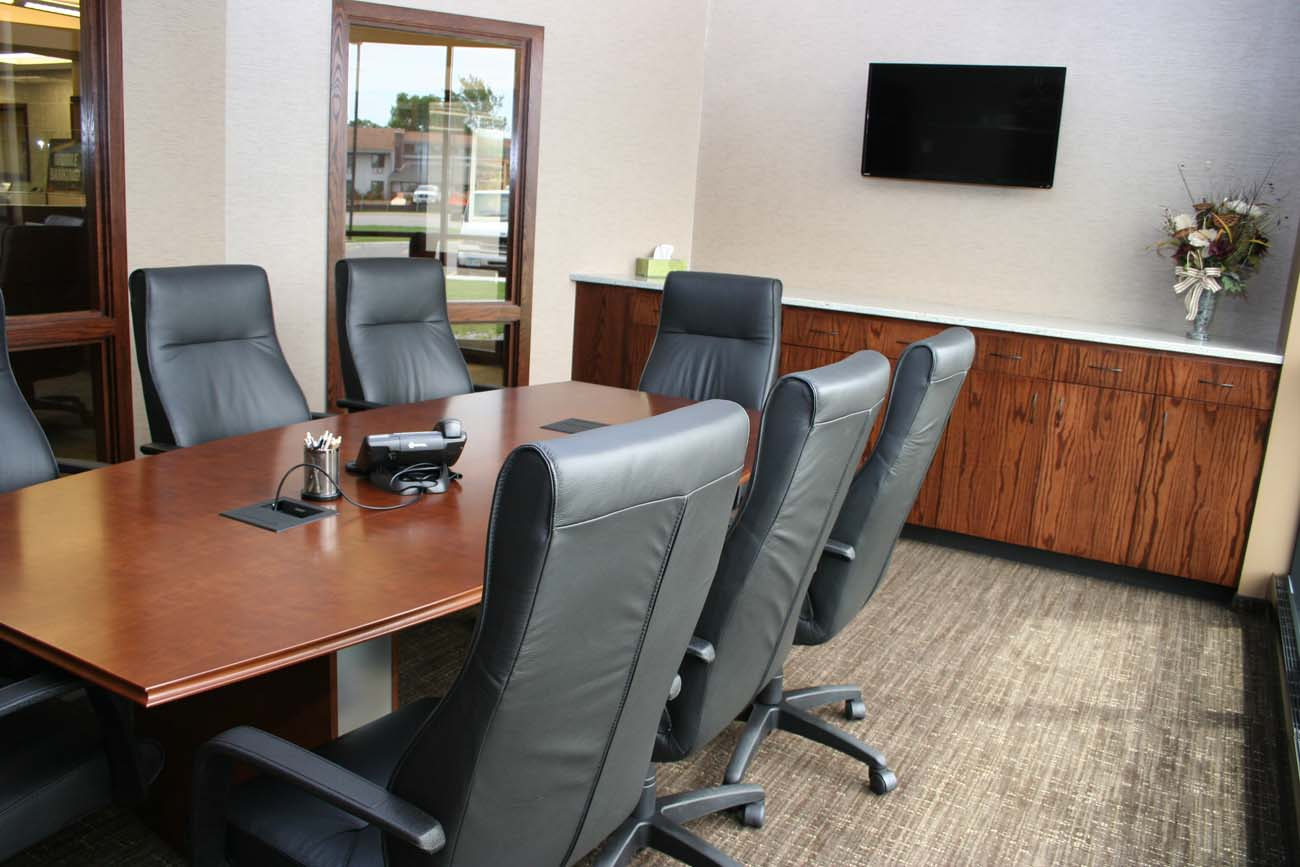 A conference room with a table and chairs and a flat screen tv on the wall.