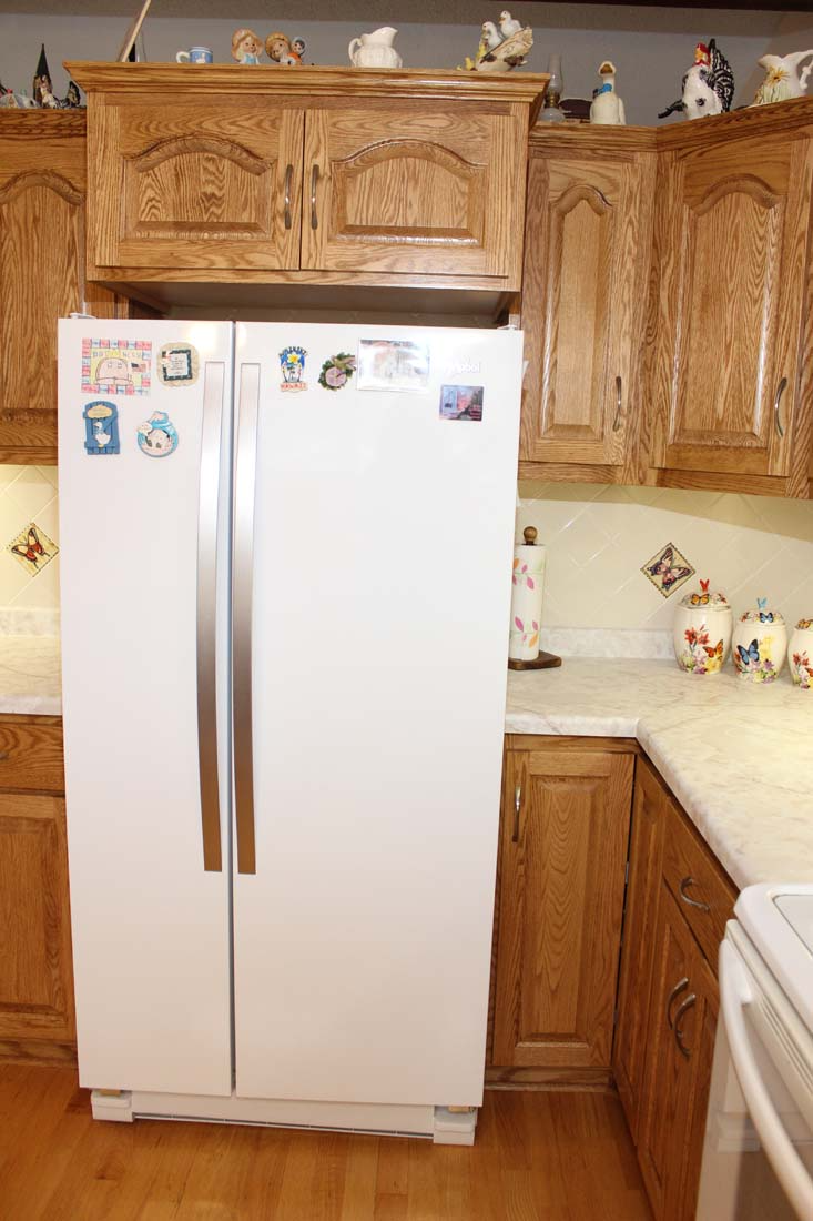 A white refrigerator is sitting in a kitchen with wooden cabinets.