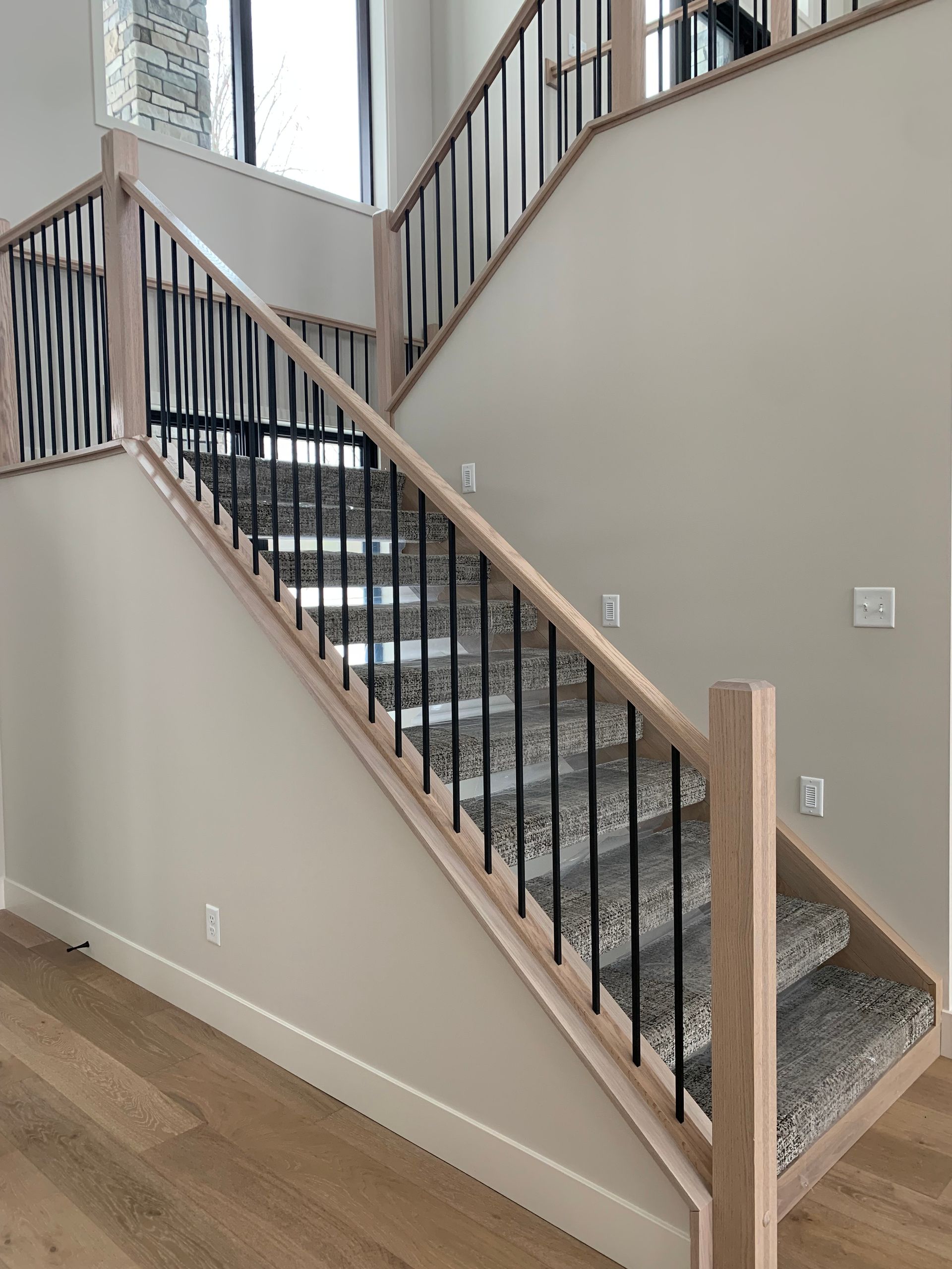 Carpeted staircase with black metal railing and light wood handrails in a beige interior.
