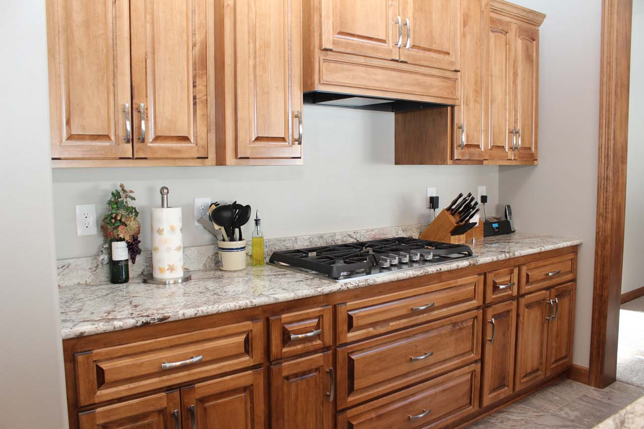 A kitchen with wooden cabinets , granite counter tops and a stove top oven.