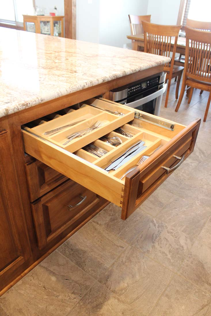 A wooden cutlery drawer is open in a kitchen.