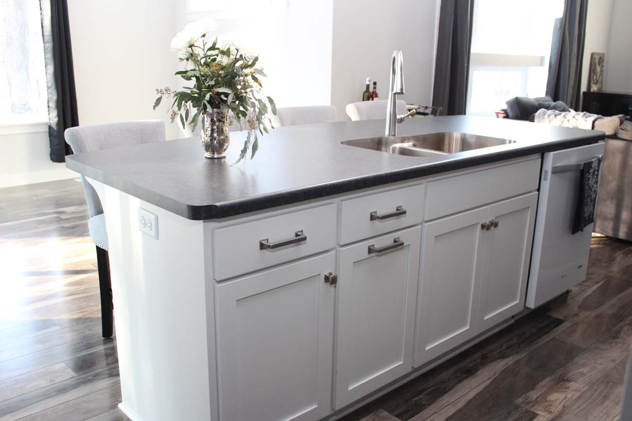 A kitchen with white cabinets , a sink , and a vase of flowers on the counter.