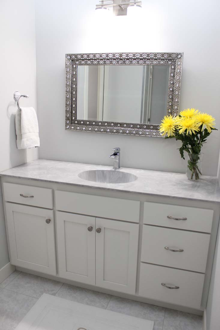 A bathroom with a sink , mirror and vase of flowers.