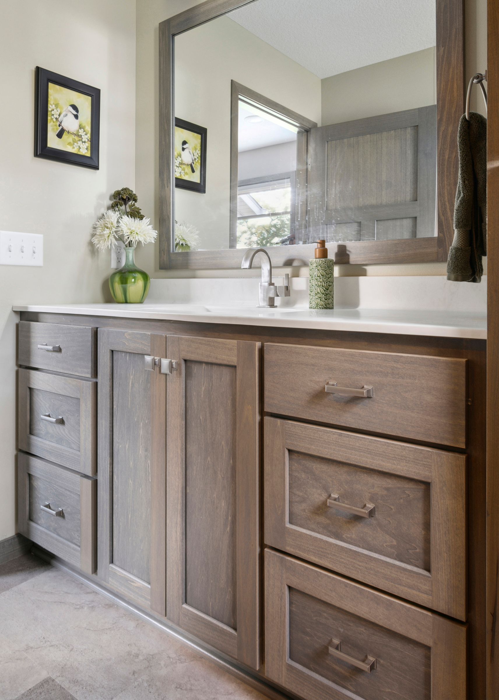 Modern bathroom vanity with wood cabinets, white countertop, mirror, and wall decor