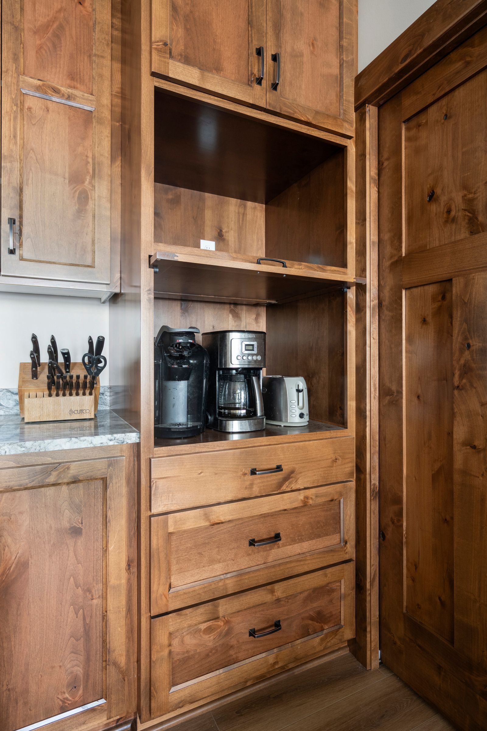 Wooden kitchen cabinet with coffee maker, coffee grinder, and utensil holder on the counter