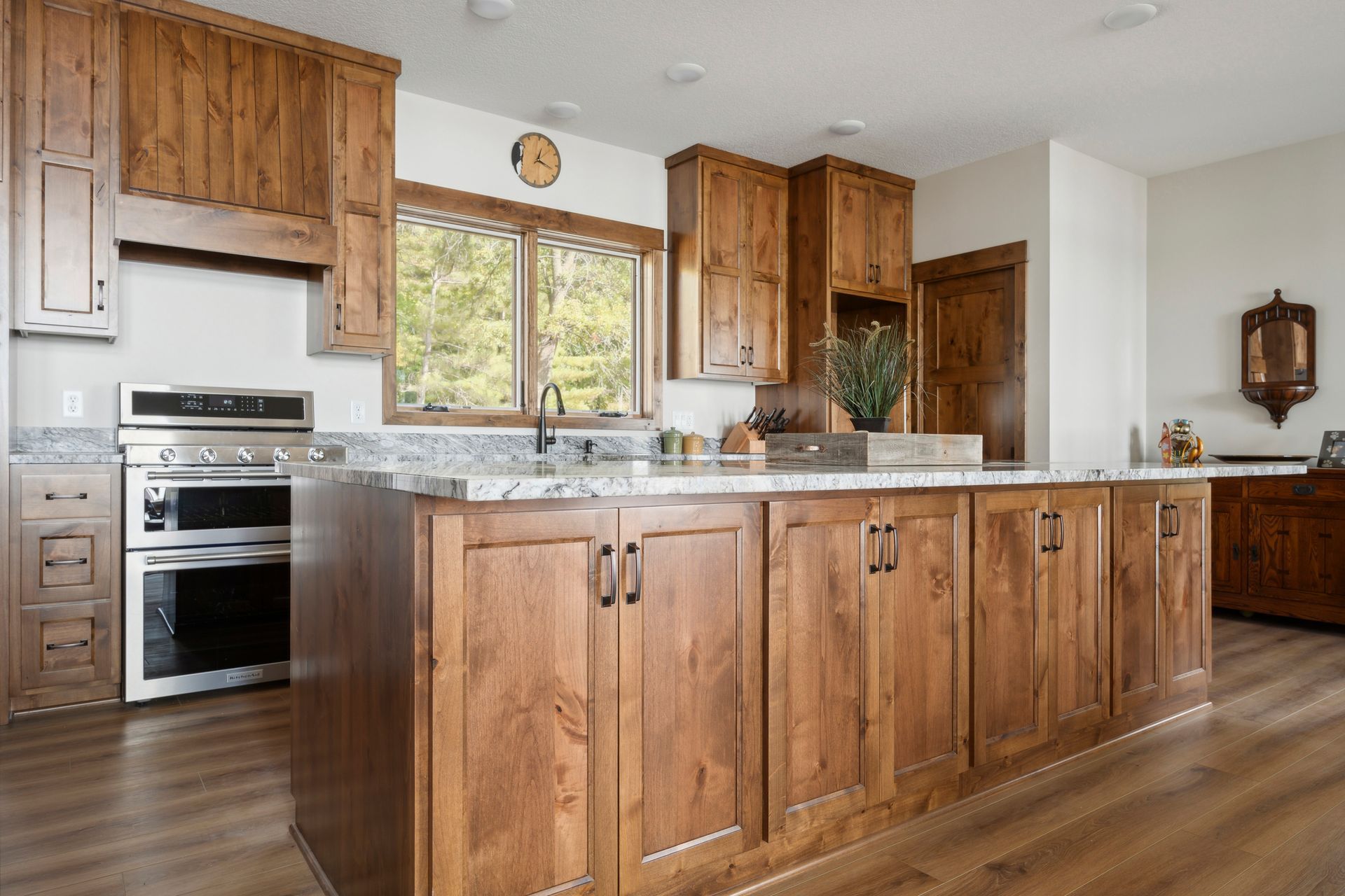 Warm kitchen with wooden cabinets, stainless steel oven, large island, and window above the sink.
