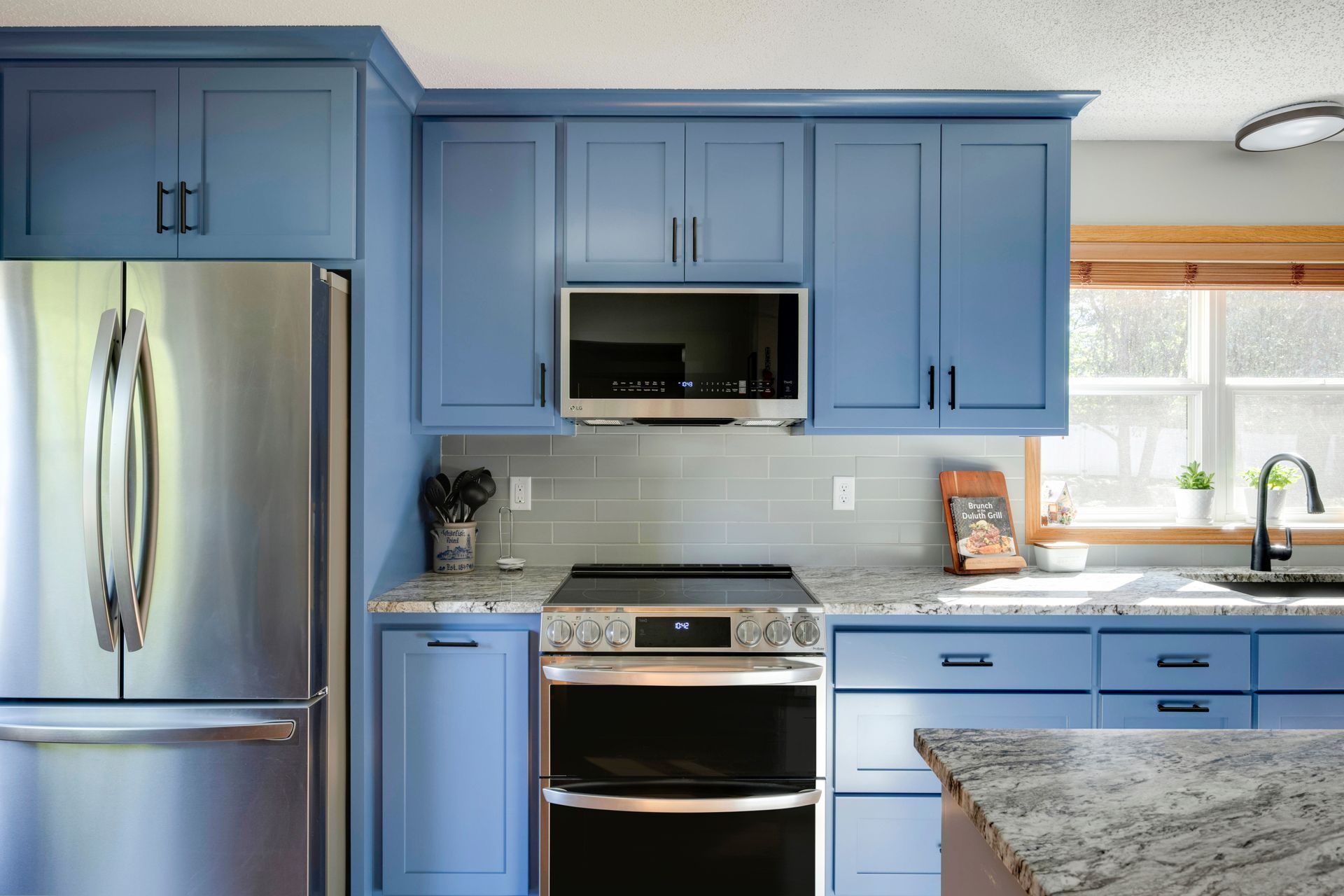 Blue kitchen with stainless steel appliances, white backsplash, and granite countertops