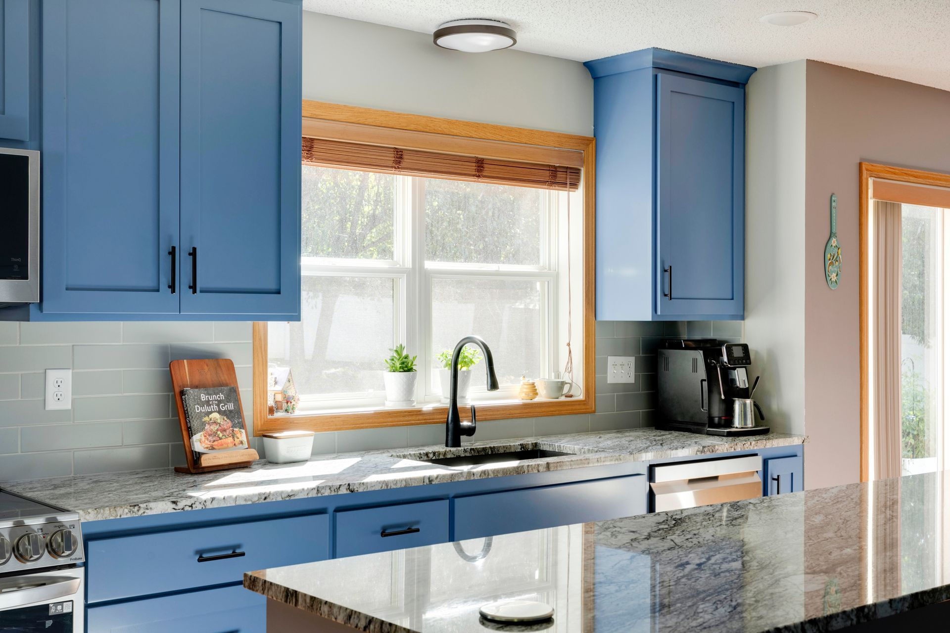 Bright blue kitchen with granite island, sink under window, and coffee maker on the counter.