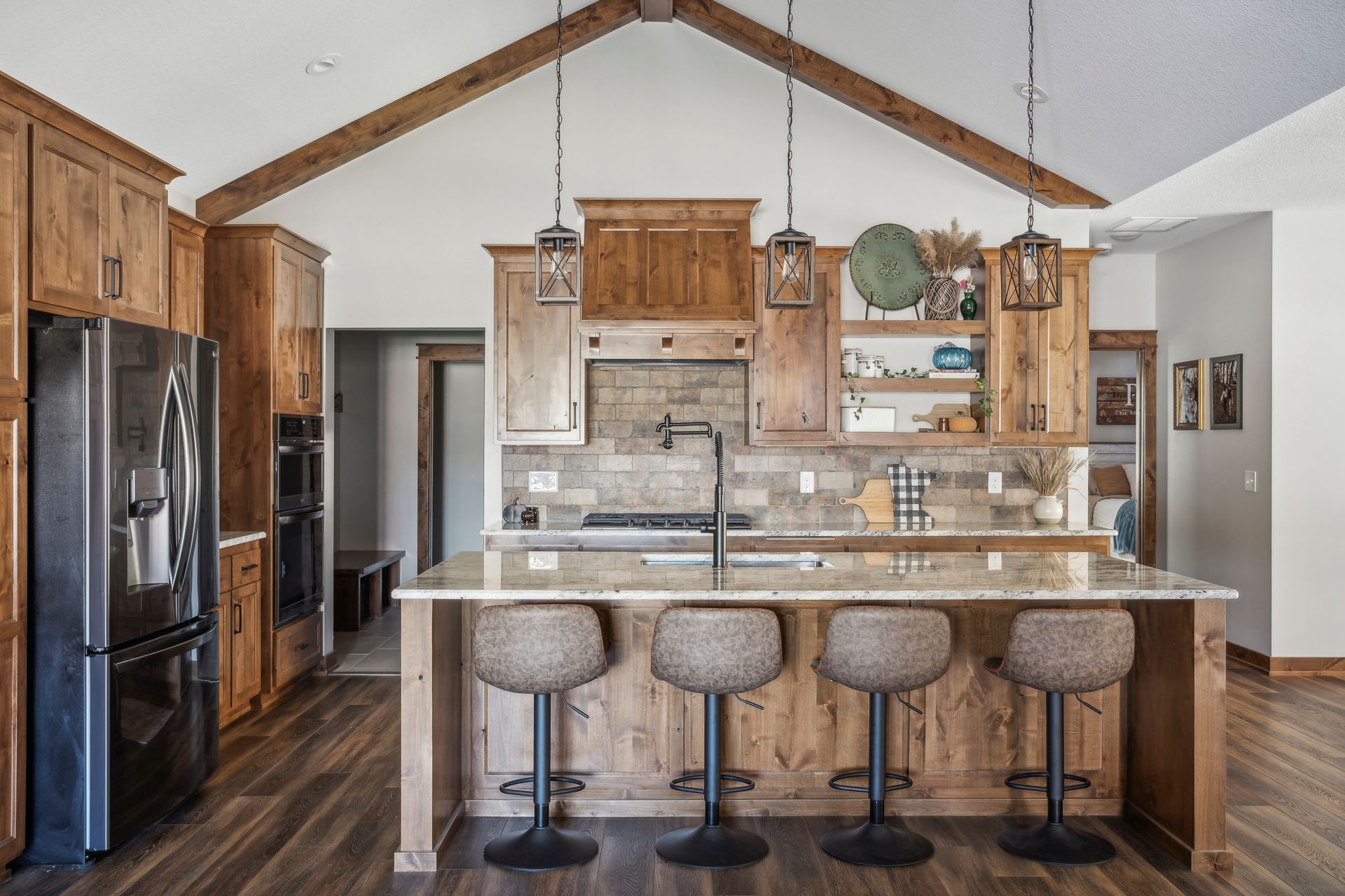 Spacious rustic kitchen with wood cabinets, large island, and four bar stools beneath vaulted ceiling.