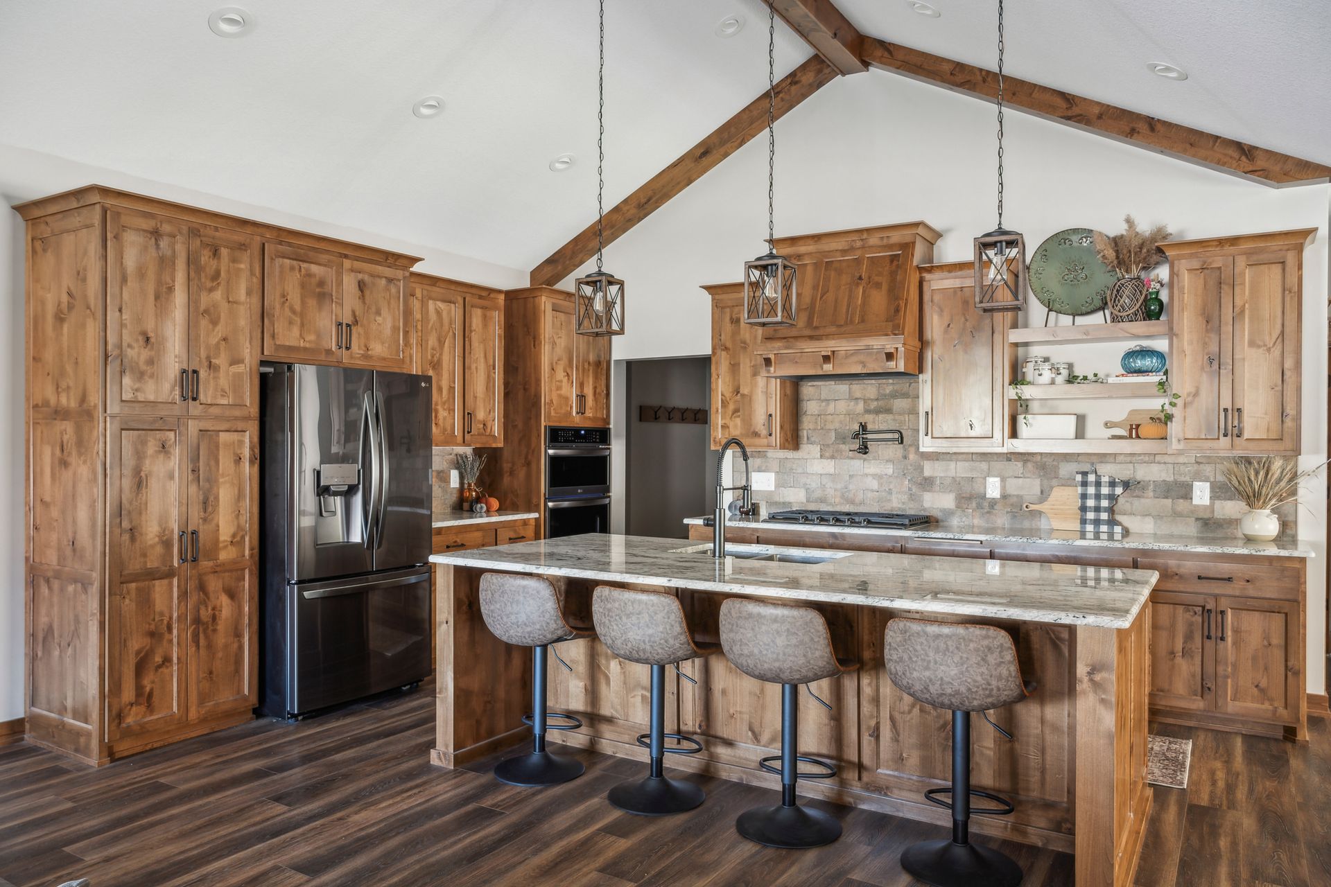 Rustic kitchen with wood cabinets, stainless fridge, and marble island with four stools