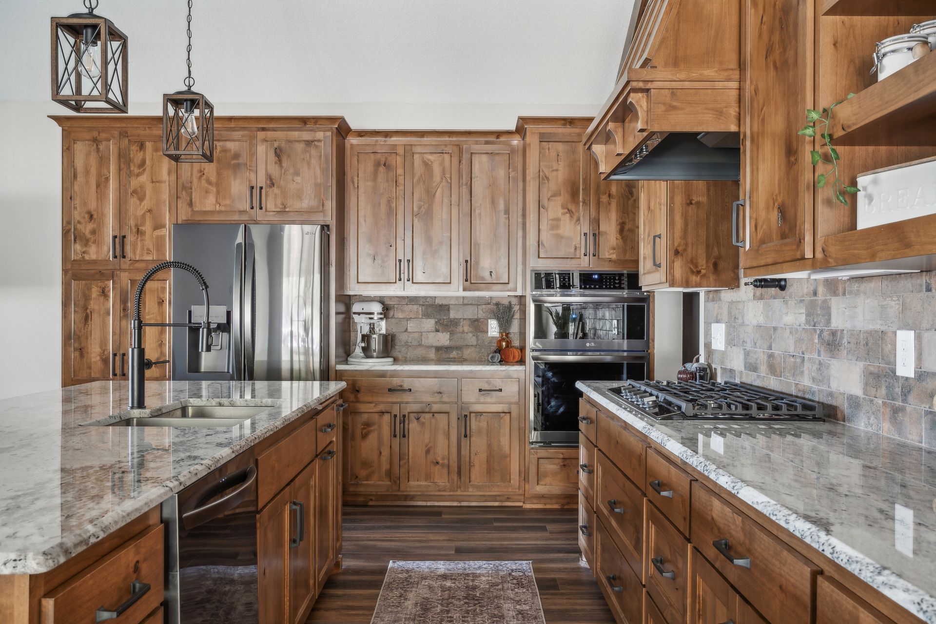 Rustic kitchen with wood cabinets, marble counters, stainless appliances, and pendant lights