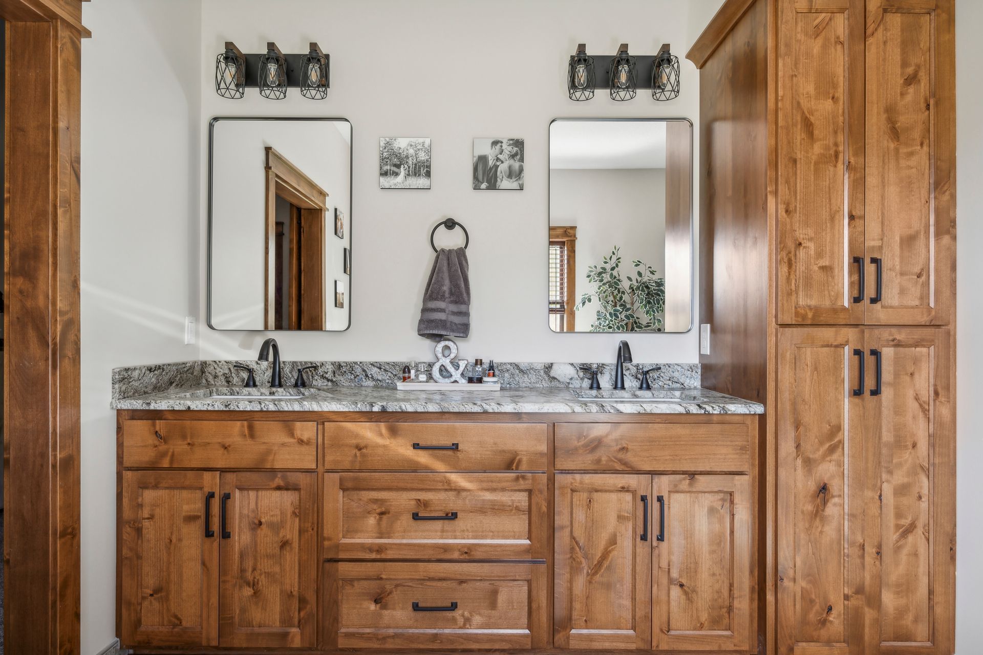 Wooden bathroom vanity with double mirrors, granite countertop, and wall sconces