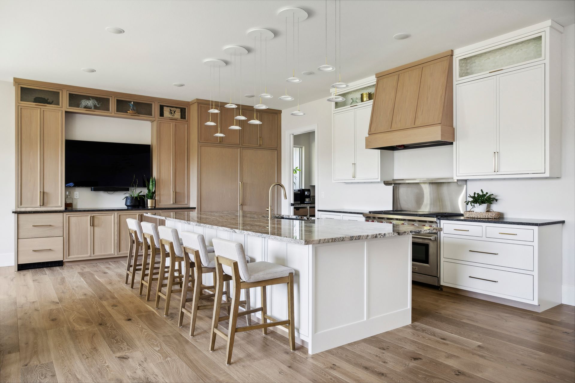Modern white kitchen with island seating, wood floors, built-in cabinets, and stainless steel appliances
