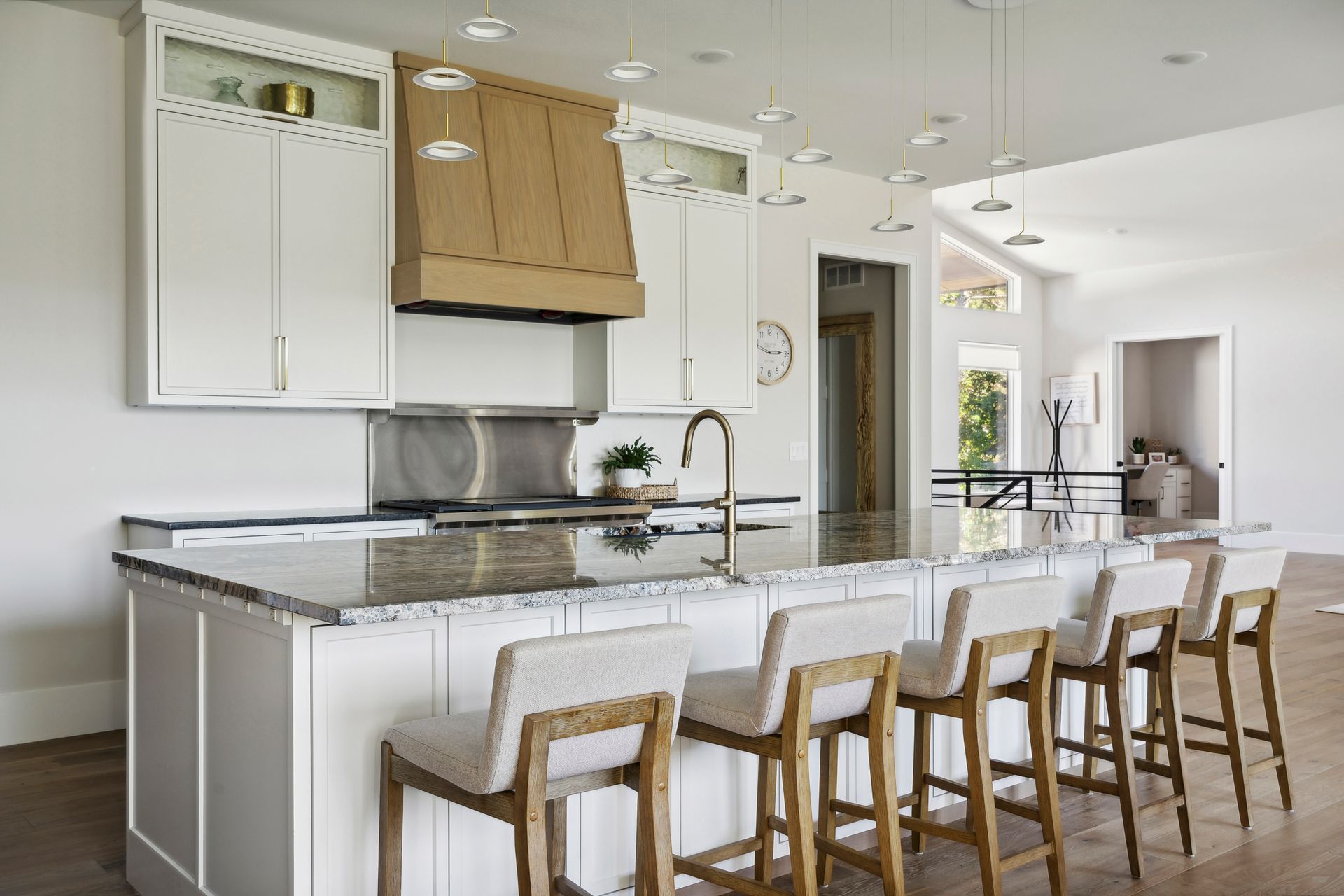Modern white kitchen with island, wooden stools, stainless appliances, and light wood floors