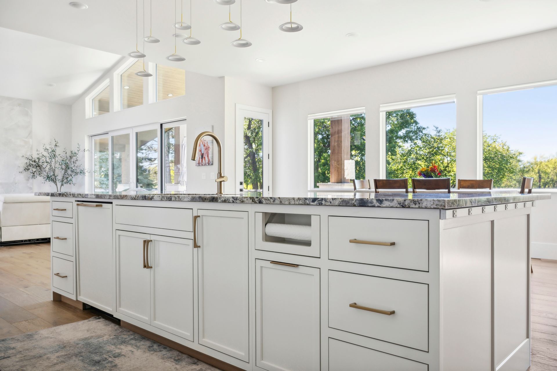 Bright modern kitchen with white cabinets, marble island, and large windows overlooking greenery