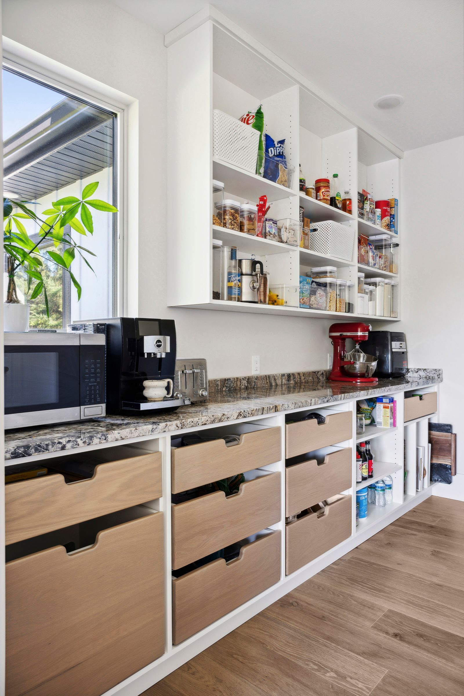 Modern kitchen with open shelving, coffee maker, and wooden cabinets under a window