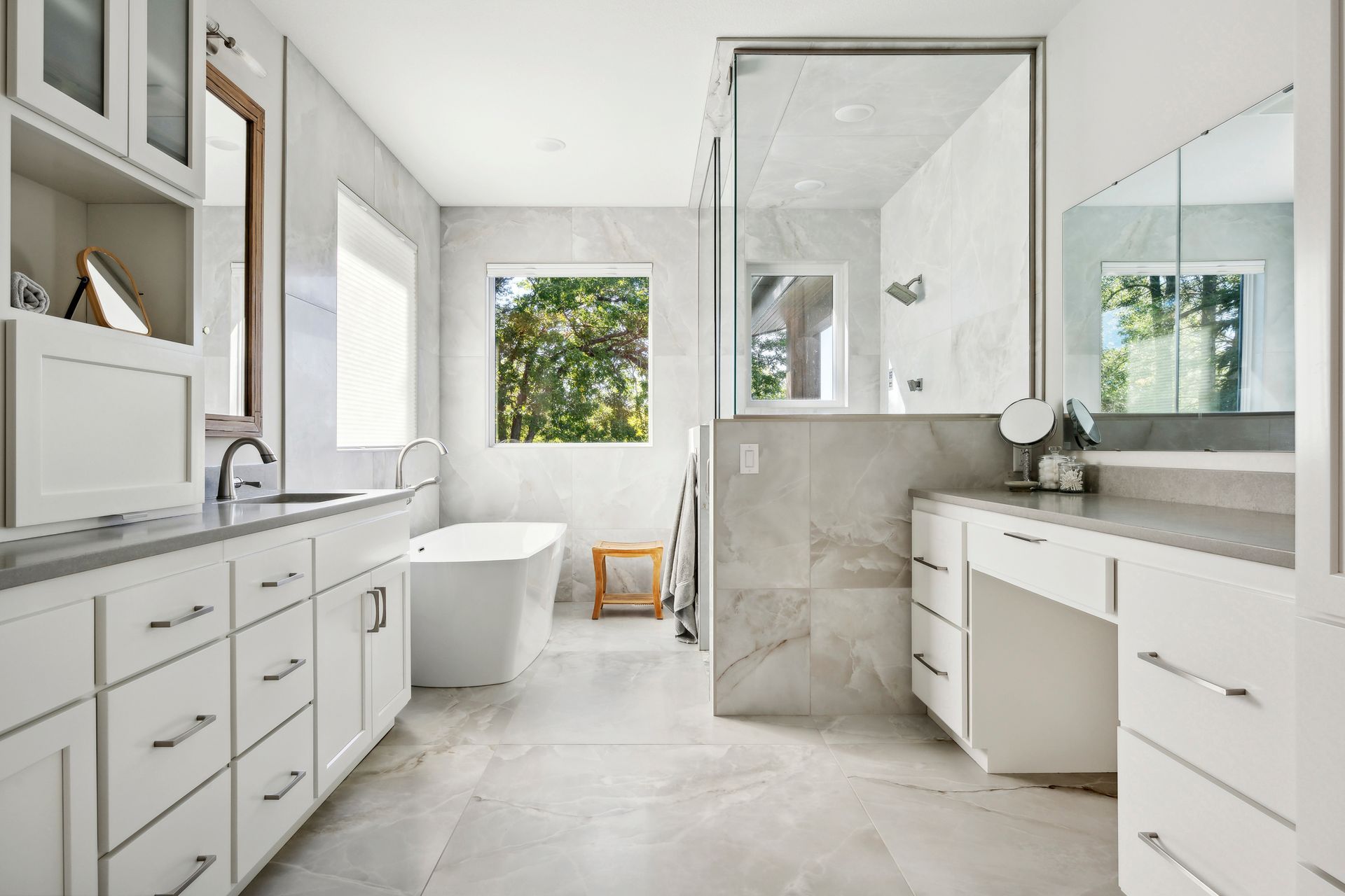 Bright modern bathroom with double vanity, freestanding tub, glass shower, and large window looking outside
