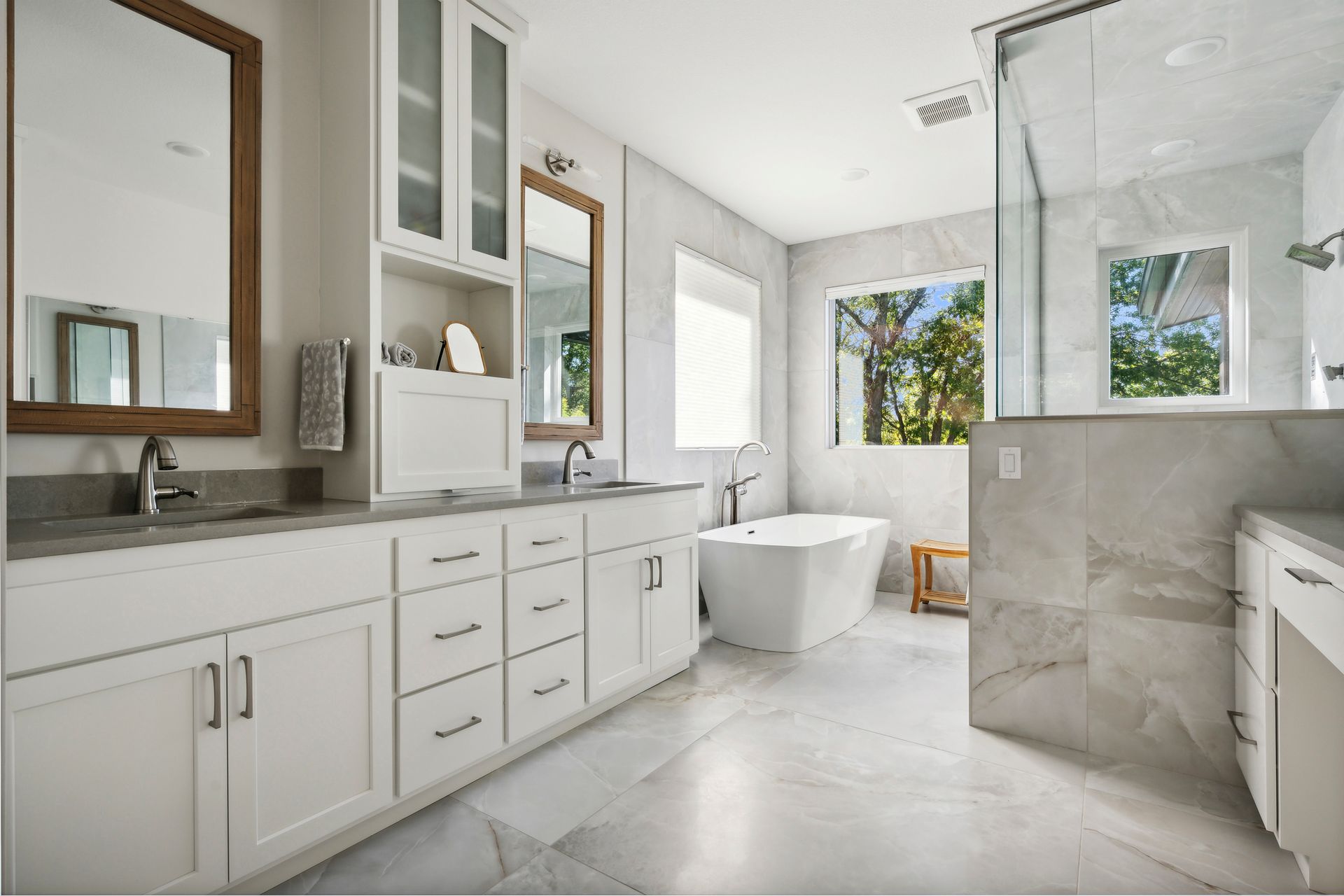 Bright modern bathroom with double vanity, freestanding tub, and marble tile walls and floor