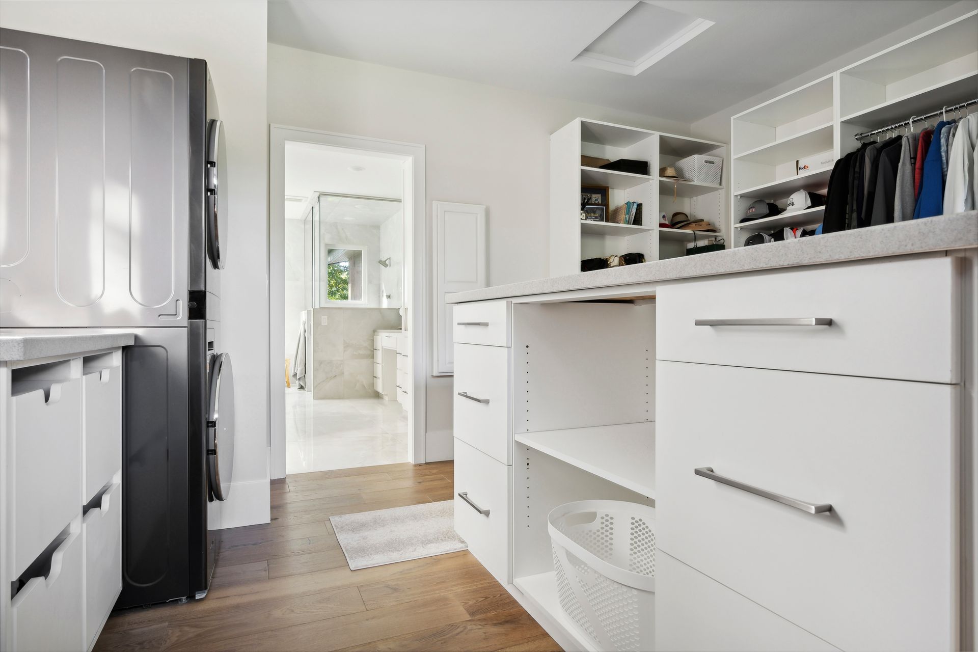 Bright white walk-in closet with drawers, shelves, hanging clothes, and a doorway to a bathroom.