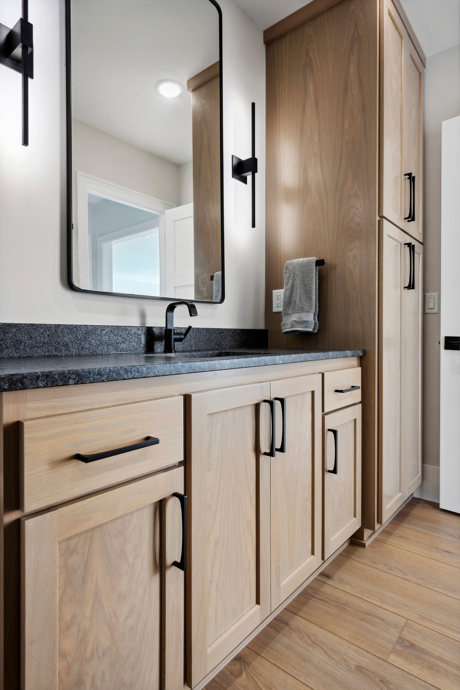 Modern bathroom vanity with wood cabinets, black countertop, mirror, and towel rack