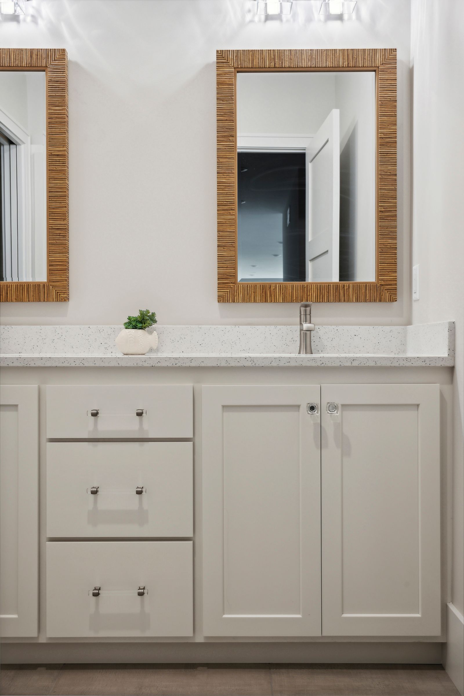 Bright bathroom vanity with white cabinets, marble countertop, and wood-framed mirror above a chrome faucet.