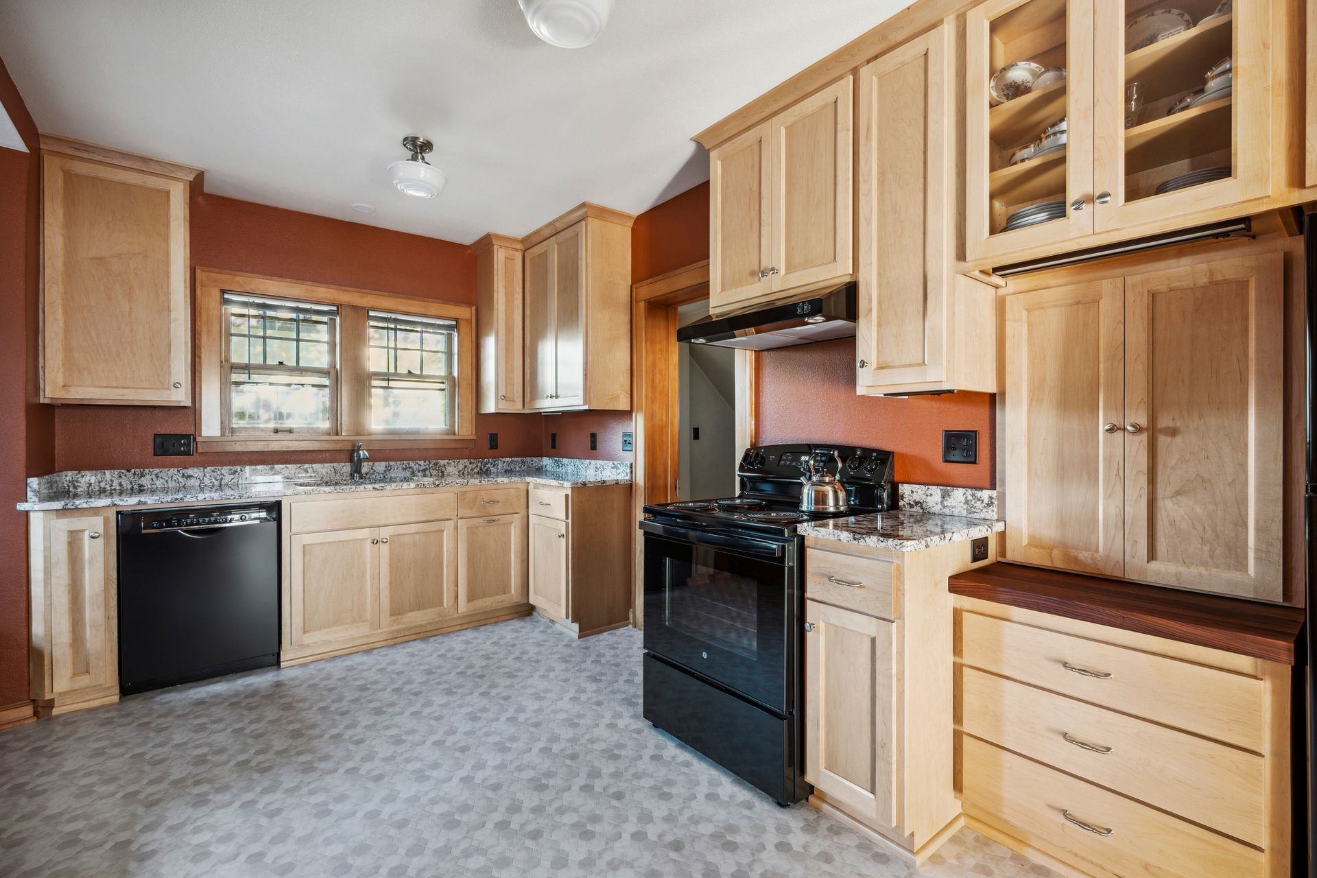 Spacious kitchen with light wood cabinets, black appliances, tiled floor, and a window over the sink