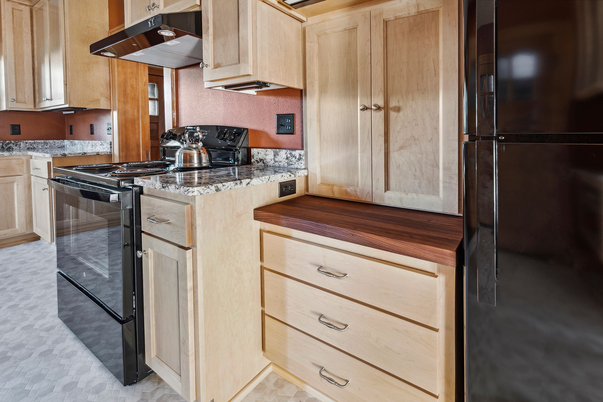 Wooden kitchen with black appliances, beige cabinets, and a dark refrigerator in the corner.