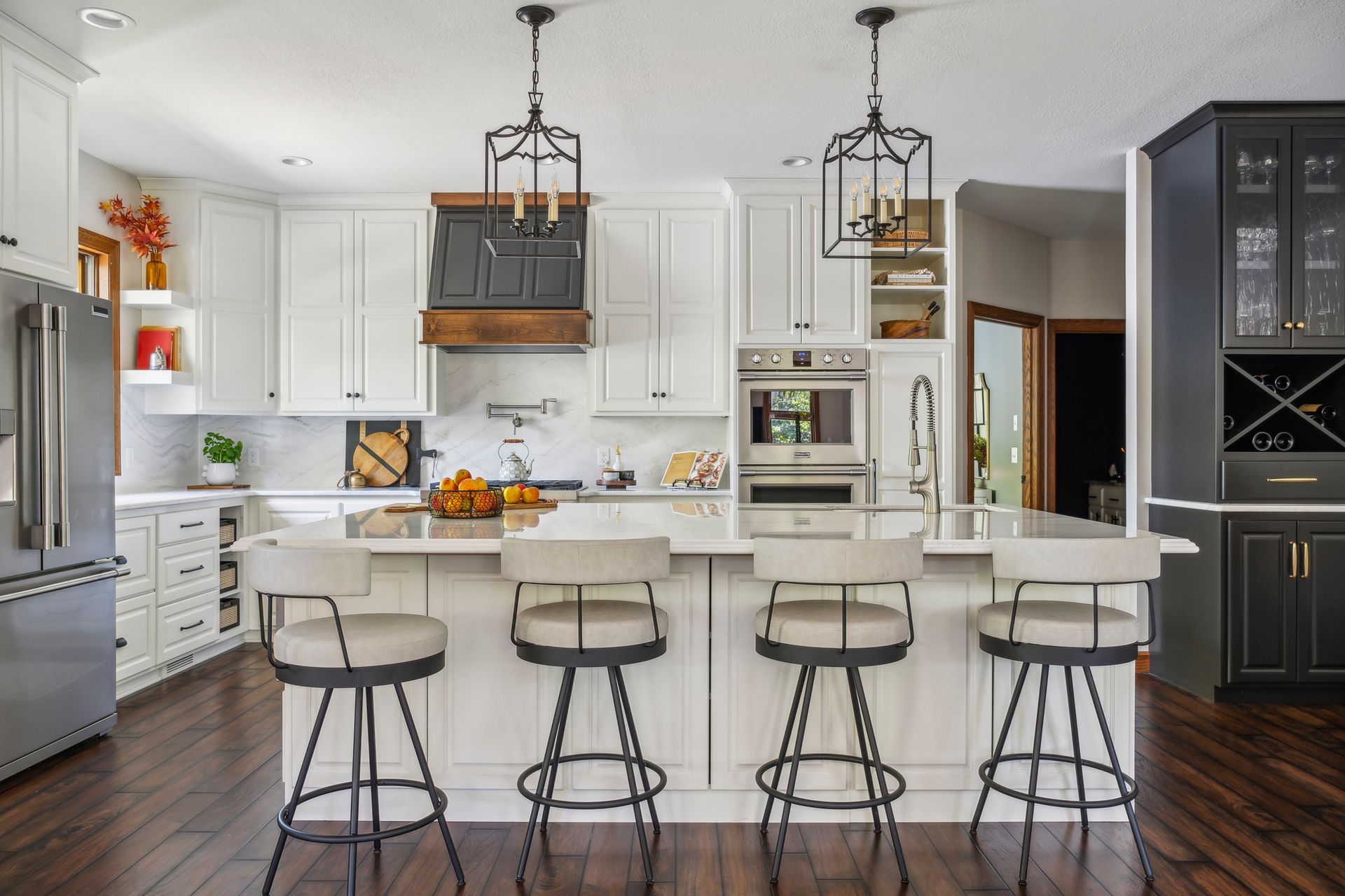 Modern white kitchen with black island, four stools, pendant lights, and dark wood floors