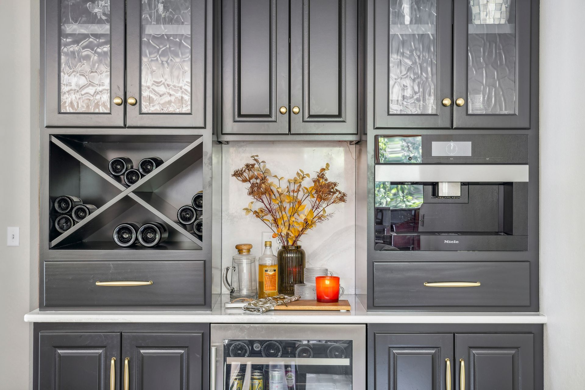Gray built-in cabinets with glass doors, wine rack, and decorative vases on a kitchen counter.