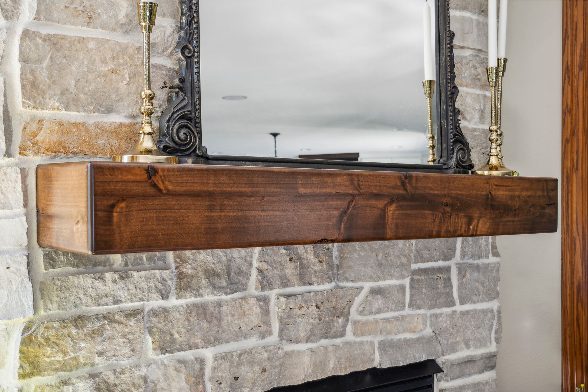 Wooden mantel shelf beneath an ornate mirror on a stone fireplace wall