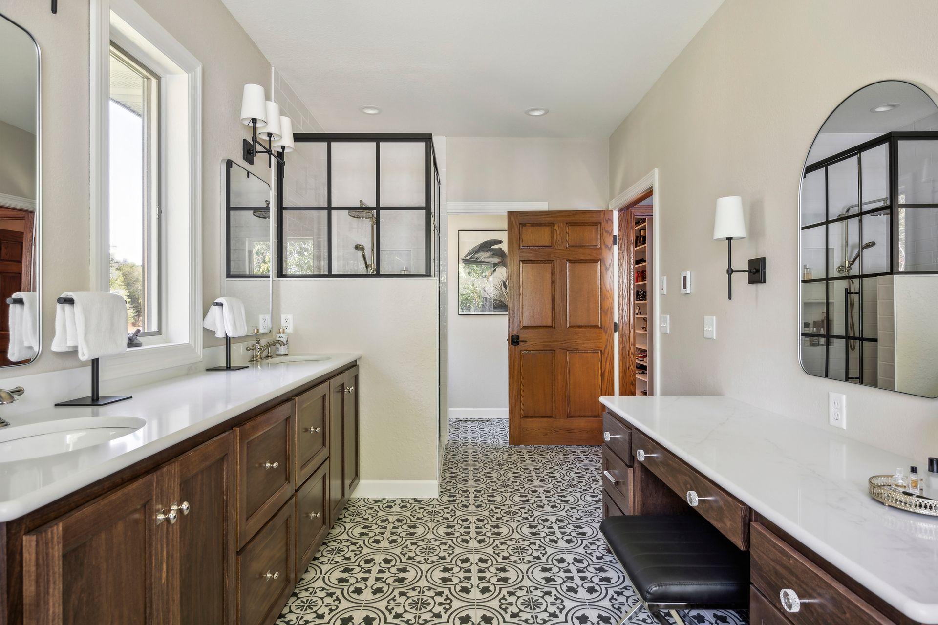 Modern bathroom with patterned tile floor, dark wood vanity, long counter, and glass shower partition.