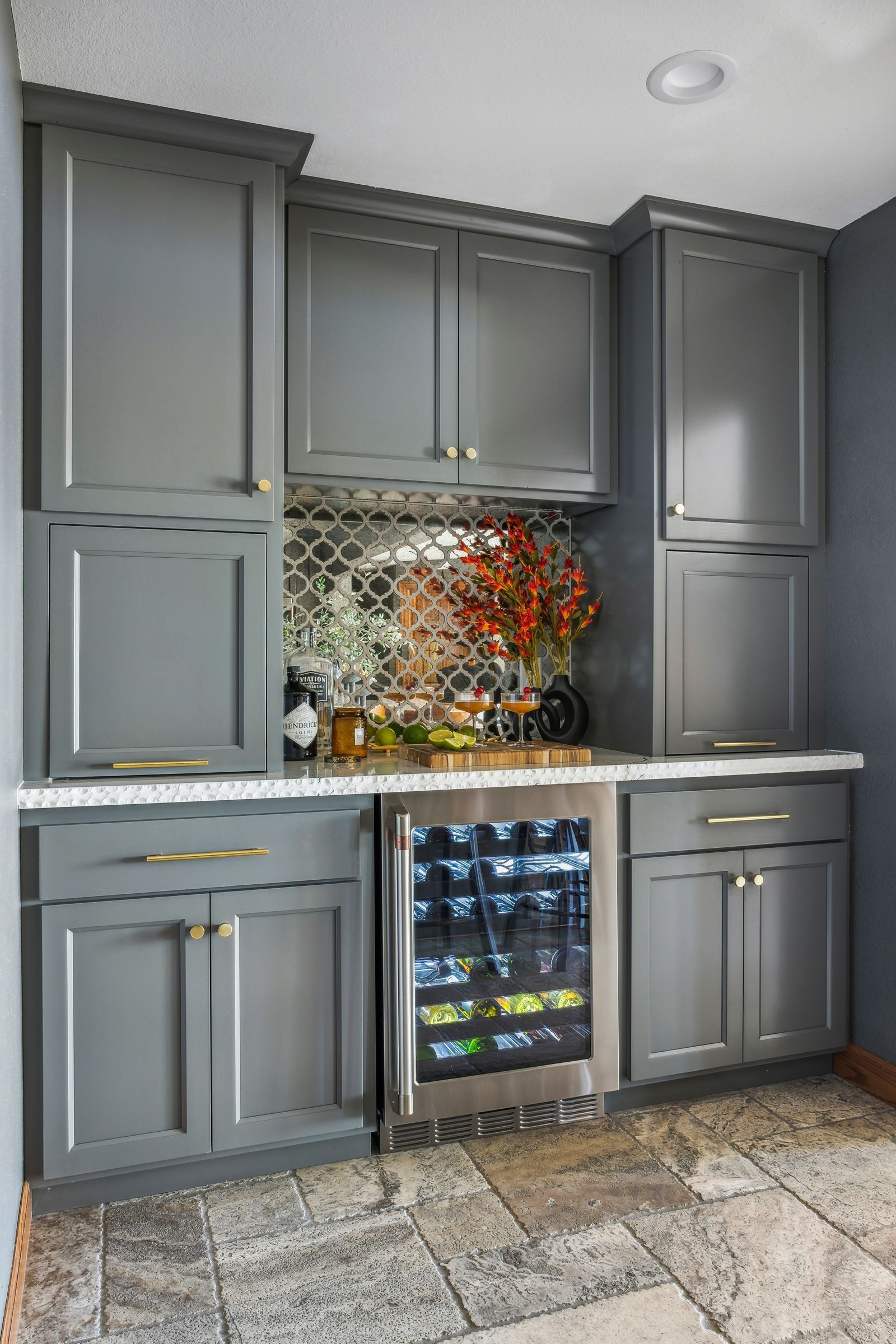 Gray kitchen cabinet wall with built-in mini fridge, mosaic backsplash, and orange flowers on the counter