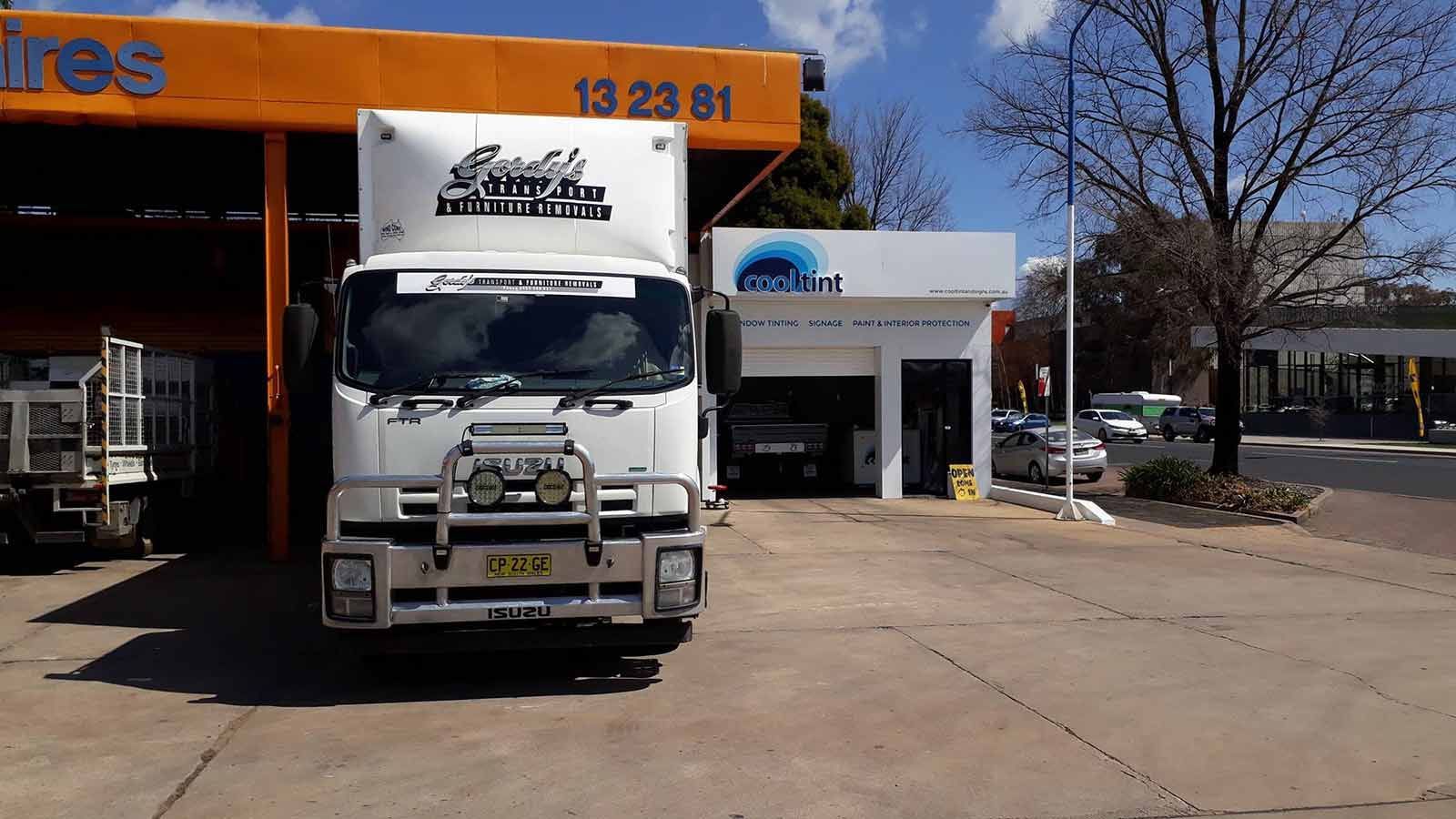 A White Truck Is Parked In Front Of A Building That Says Tires — Gordy's Furniture Removals in Bathurst, NSW