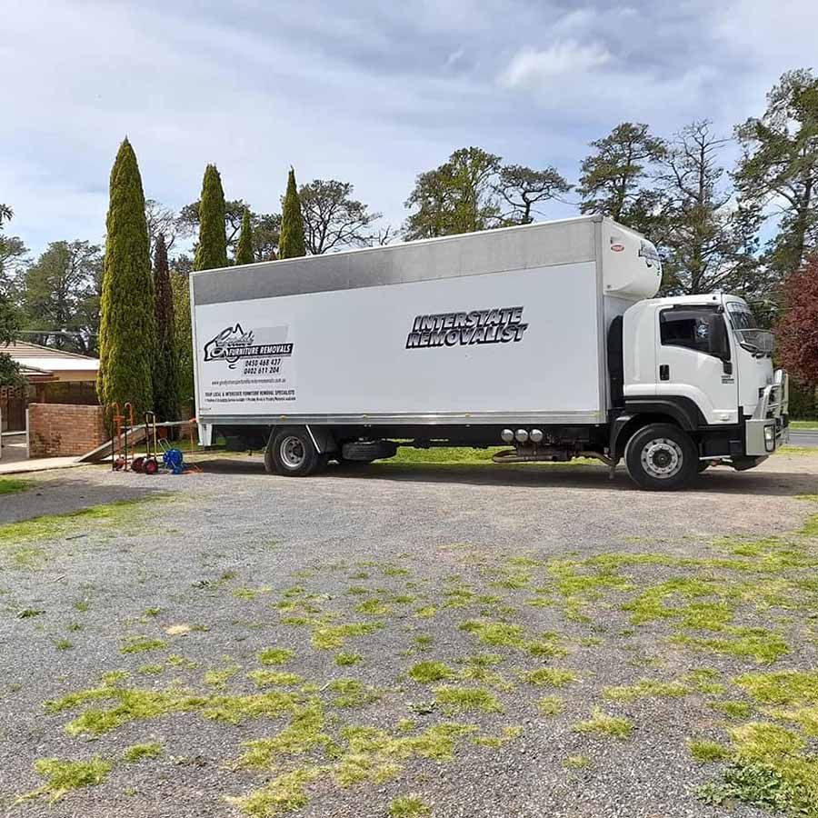 A White Moving Truck Is Parked In A Gravel Lot — Gordy's Furniture Removals in Bathurst, NSW
