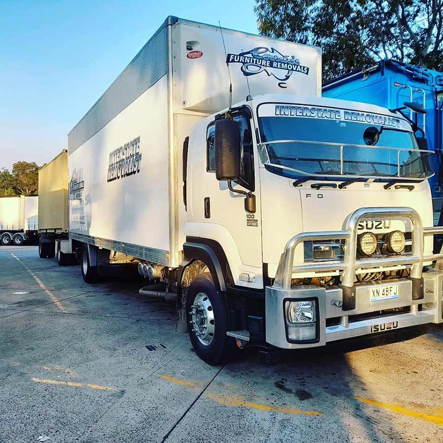 A White Truck Is Parked In A Parking Lot Next To A Blue Building — Gordy's Furniture Removals in Bathurst, NSW