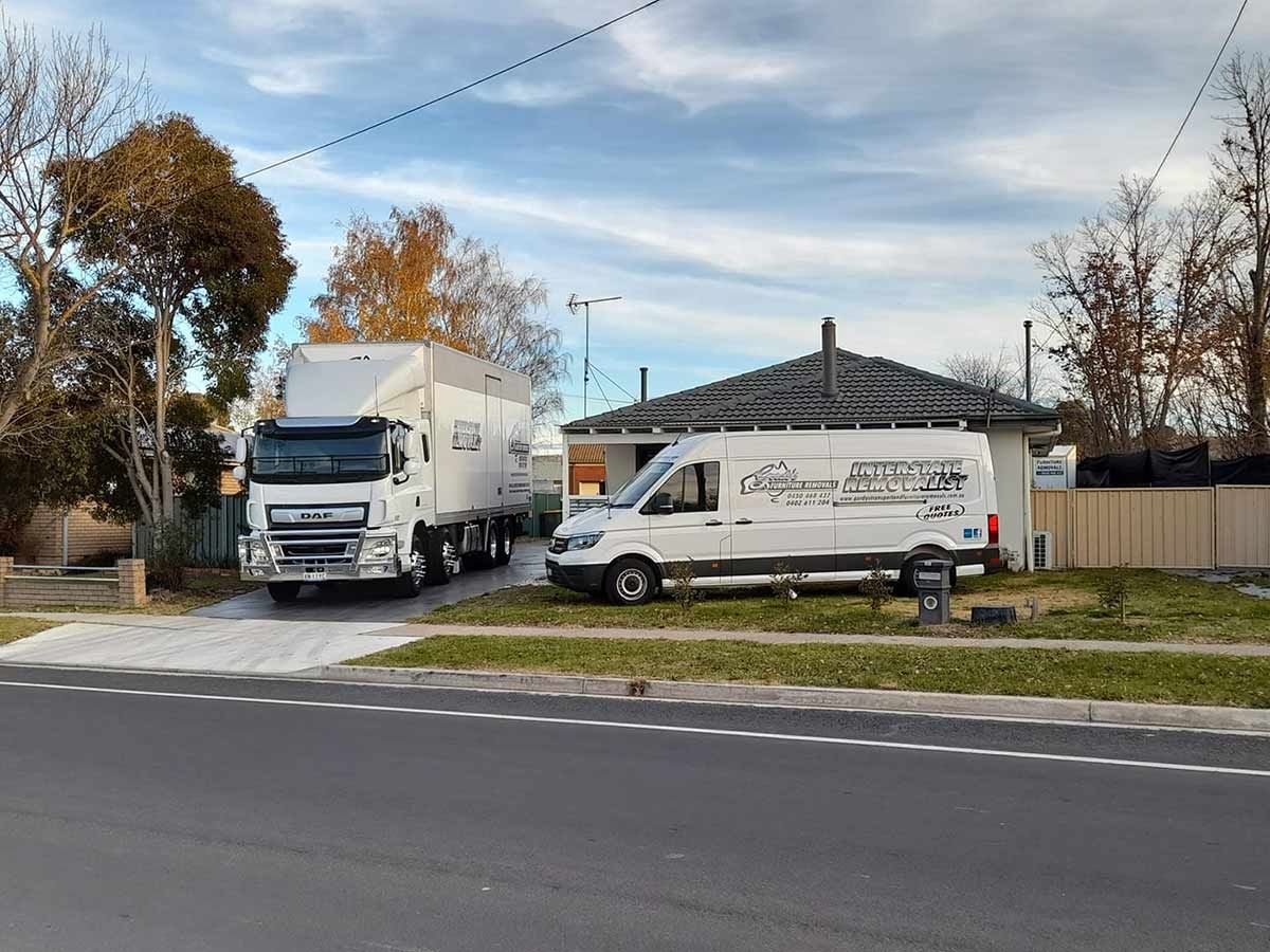 Two Trucks And A Van Are Parked In Front Of A House — Gordy's Furniture Removals in Bathurst, NSW