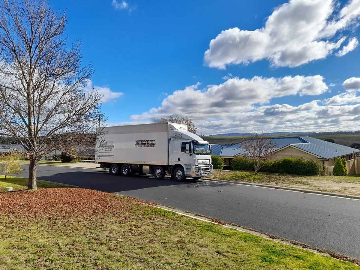 A White Truck Is Driving Down A Street Next To A Lake — Gordy's Furniture Removals in Bathurst, NSW