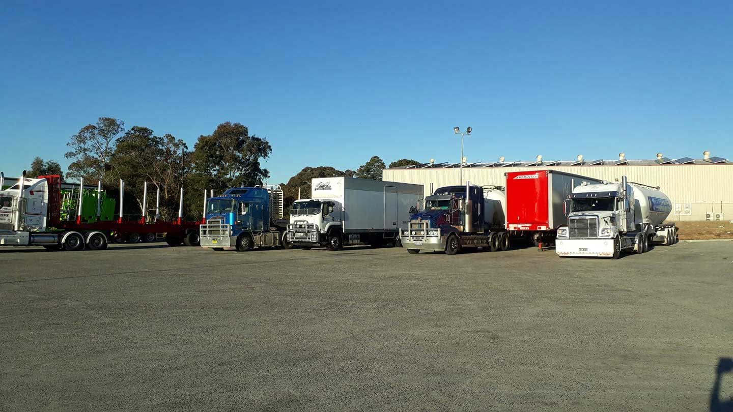 A Row Of Semi Trucks Are Parked In A Gravel Lot — Gordy's Furniture Removals in Bathurst, NSW