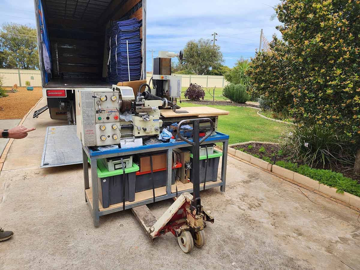 A Man Is Pushing A Cart With A Machine On It In Front Of A Truck — Gordy's Furniture Removals in Bathurst, NSW