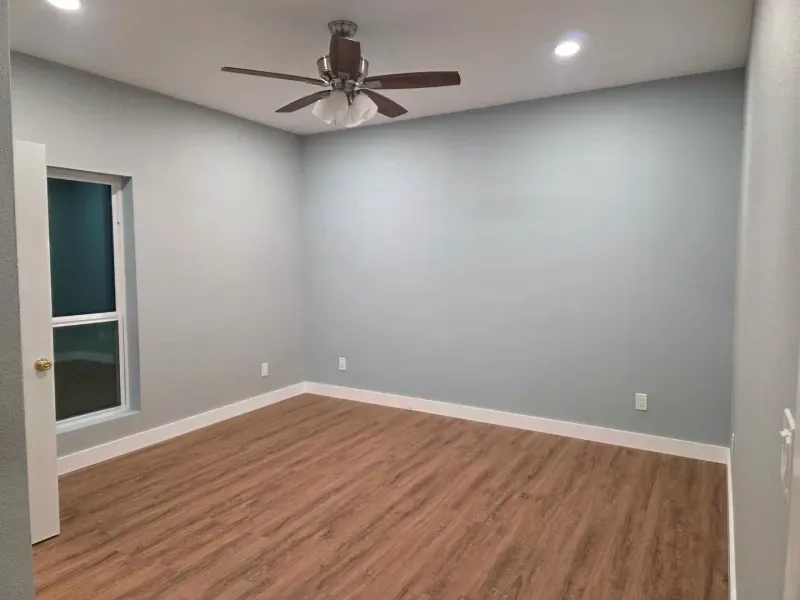 Empty bedroom with gray walls, wood-look floor, ceiling fan, and a window on the left.